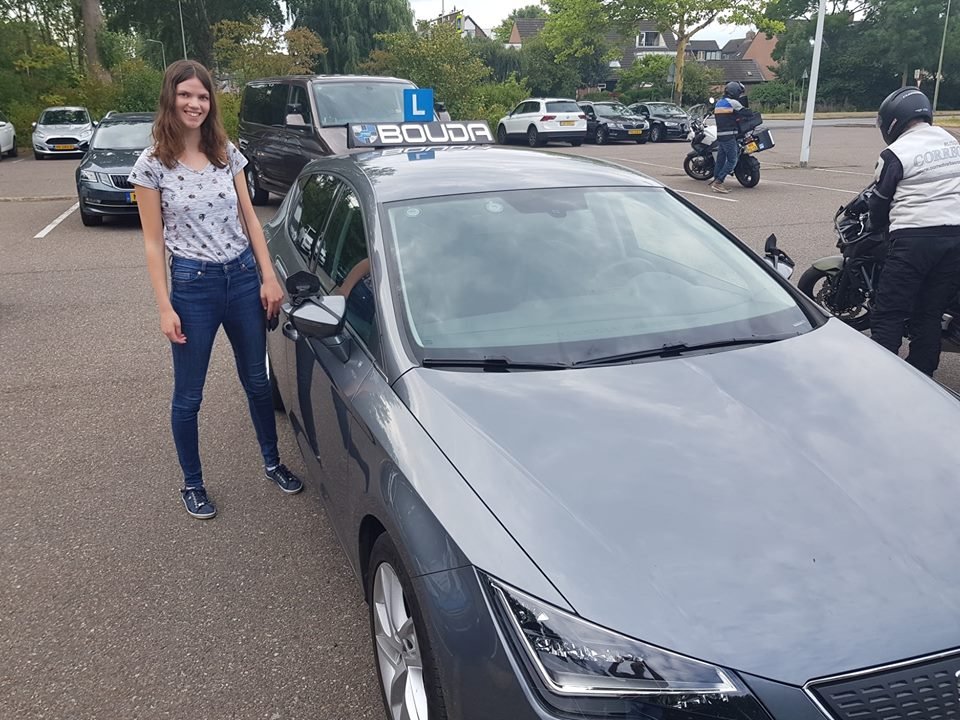 Geslaagde leerling bij een grijze lesauto van Rijschool Bouda