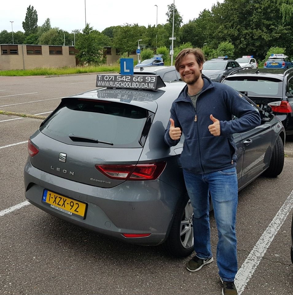 Geslaagde leerling met duimen omhoog naast de lesauto