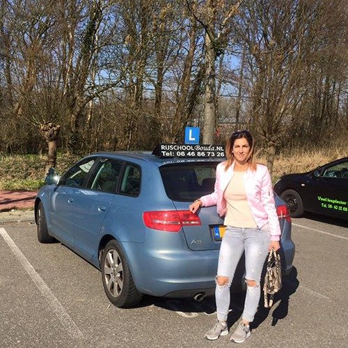 Geslaagde leerling naast een blauwe lesauto van Rijschool Bouda