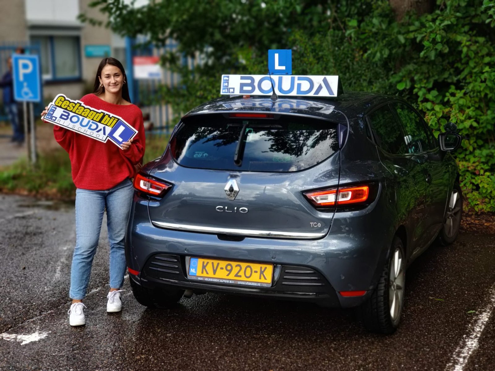 Geslaagde leerling met Bouda-bord naast de lesauto